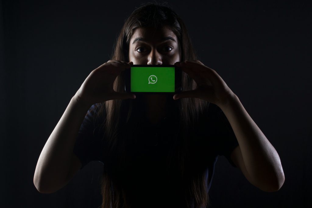 A young man holding phone displaying Whatsapp Logo
